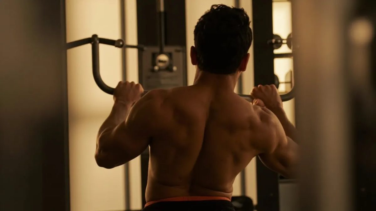 Persona diversa realizando un ejercicio de jalón al pecho en un gimnasio, iluminada con luz natural cálida