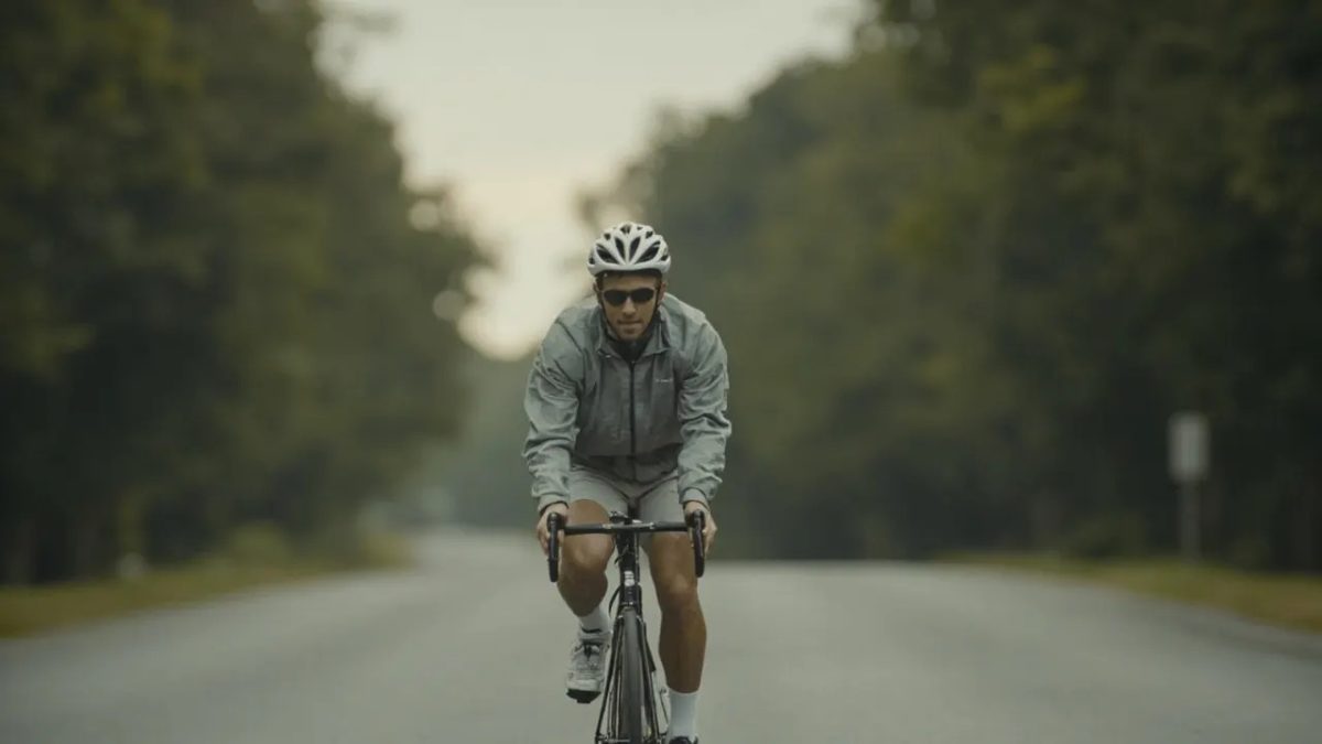 Ciclista pedaleando por una carretera arbolada a primera hora de la mañana bajo una luz suave y neutra.
