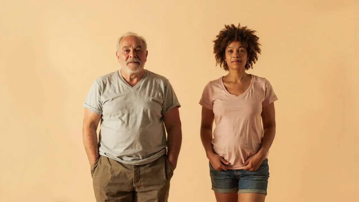 Dos personas diversas de pie una al lado de la otra en postura relajada, con cuerpos de formas distintas, bajo luz cálida y suave, sin elementos clínicos ni texto.