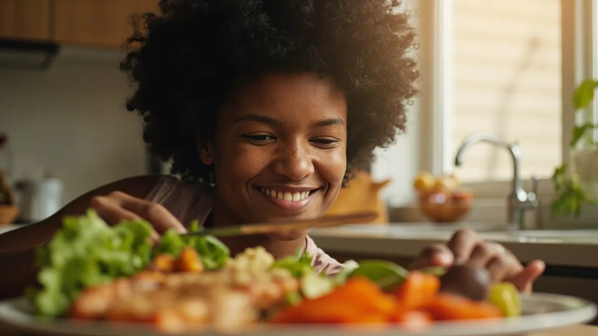 Persona diversa sonriendo mientras se dispone a comer un plato colorido y equilibrado con salmón, quinoa, verduras asadas y ensalada fresca, sobre una mesa de cocina con luz cálida natural.