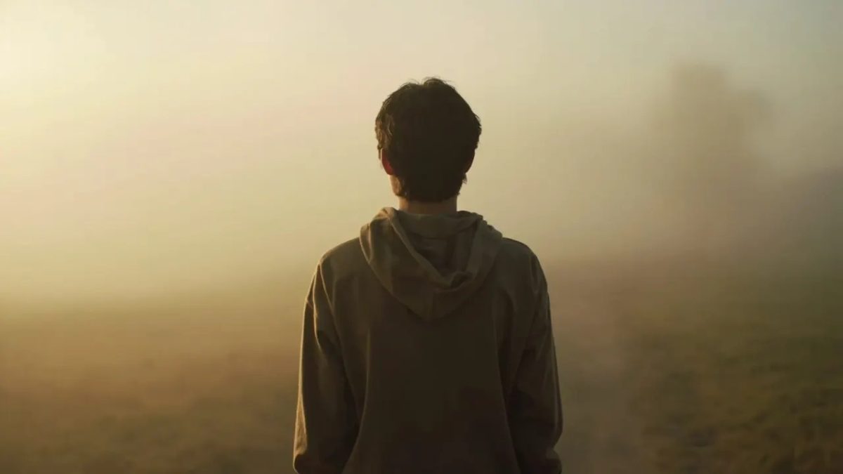 Persona diversa de espaldas deteniéndose ante una niebla densa que cubre un paisaje al amanecer, en una composición que evoca la pausa mental y la incertidumbre ante el camino.