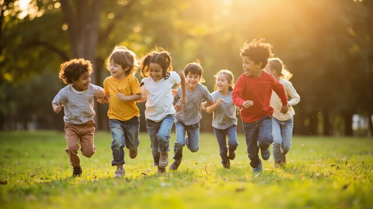 Grupo diverso de niños jugando y corriendo alegremente al aire libre en un parque soleado, vestidos con ropa cómoda.