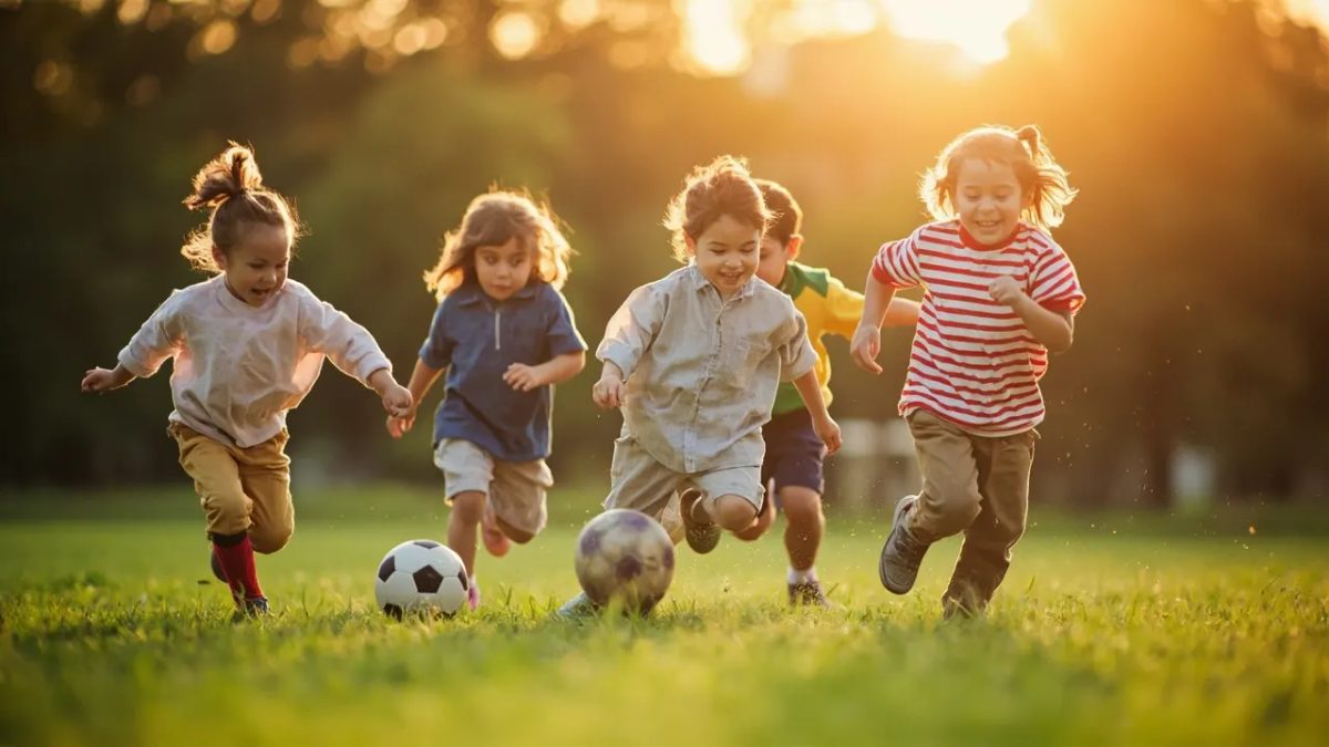 Niños diversos jugando y corriendo alegremente al aire libre en un parque verde bajo una luz cálida, practicando actividad física juntos.